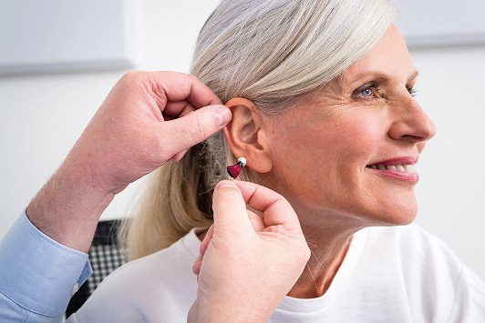 Ältere Frau bekommt ein modernes Hörgerät ins Ohr eingesetzt, Hörakustik Gesundheit.